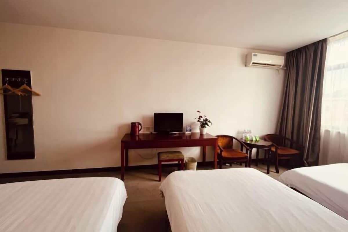 A hotel room with two beds, a desk with a television, a chair, a small table, and an air conditioning unit.