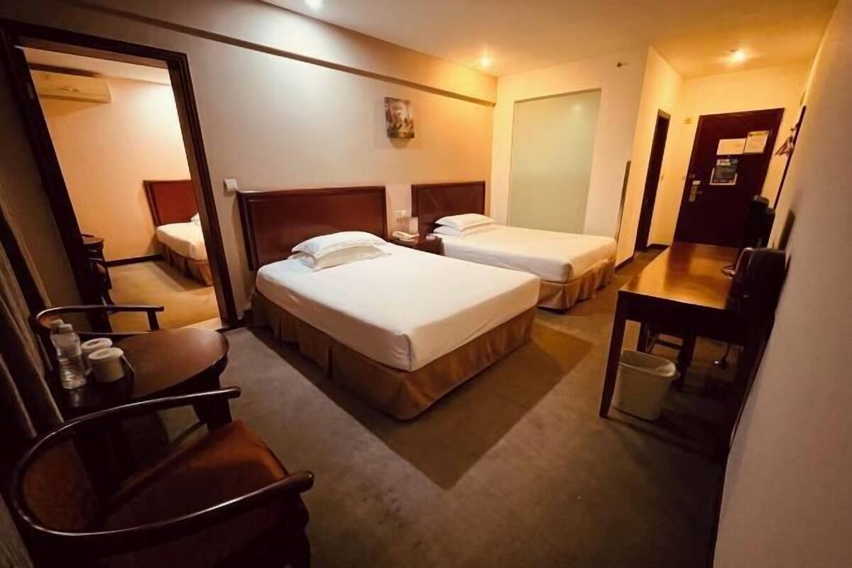 A hotel room with two beds, a desk, a chair, a trash bin, and a door.