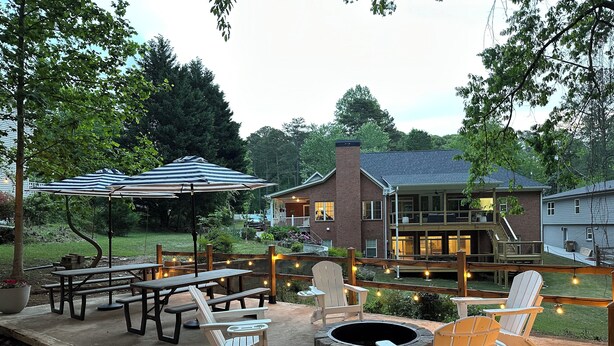 Un patio al aire libre con mesas de picnic, sillas tipo Adirondack, un brasero y luces colgantes.