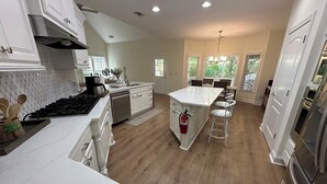 Una cocina moderna con armarios blancos, una isla central con taburetes y una estufa integrada además de un lavavajillas.