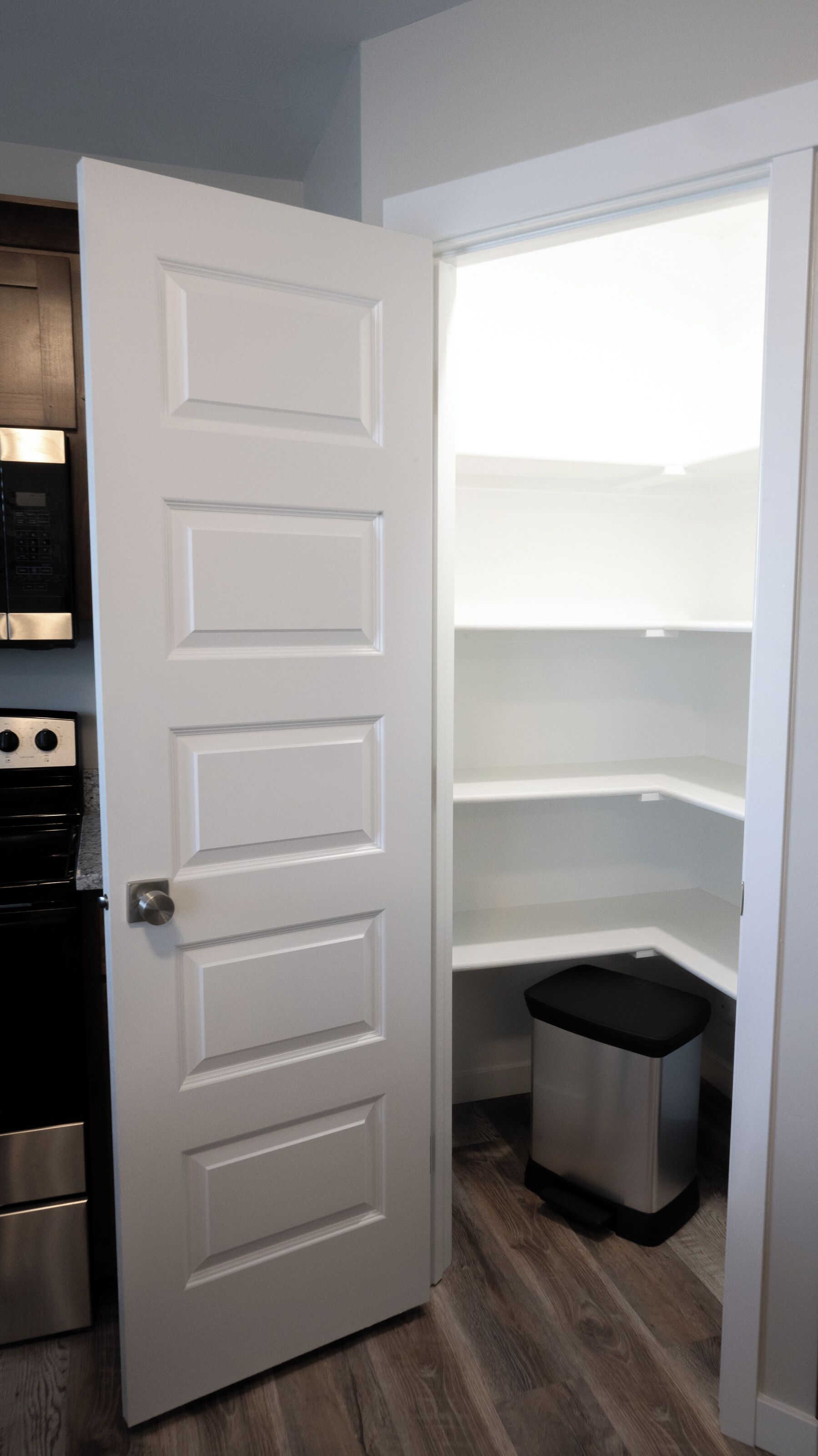 Una puerta blanca con manija de plata que da a una cocina con horno de acero inoxidable y un bote de basura negro.