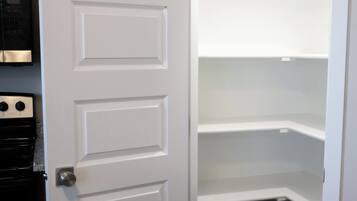 Una puerta blanca con manija de plata que da a una cocina con horno de acero inoxidable y un bote de basura negro.