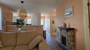 A living room with a beige sofa, a stone fireplace, and a kitchen in the background. - 1st Floor Plush Condo | W&D | Pool & Hot Tub (Myrtle Beach)