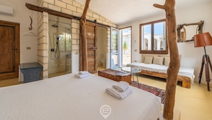 A bedroom with a large bed, a wooden bench, a small table, and a view of the outside.