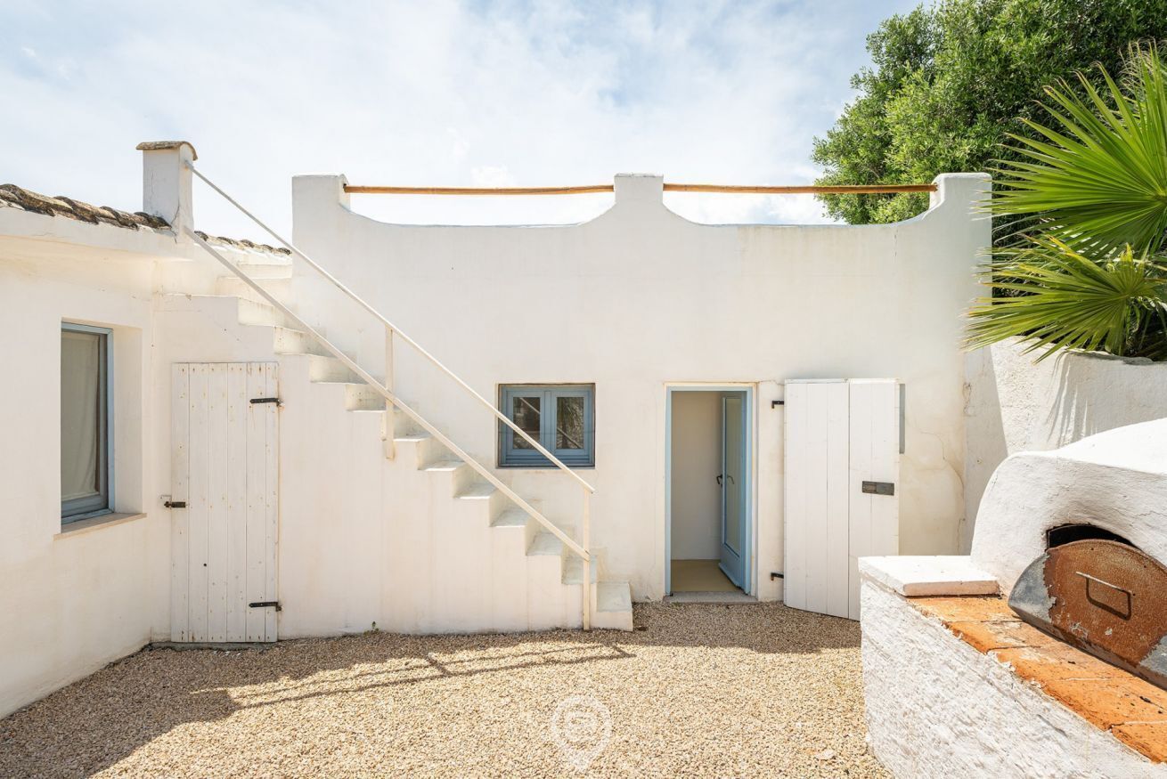A white building with a staircase leading to a door, a small window, and a brick oven.