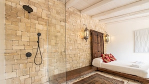 A room with a stone wall, a bed with white bedding, a wooden bench, and a patterned rug.