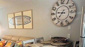 A dining area with a wooden table, woven placemats, and a wall clock. - BEACHFRONT w heated pool, steps to sand. Winter discounts Bath remodel 2 BR 1 BA (Gulf Shores)