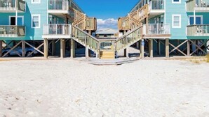 A beachfront property with two-story buildings featuring balconies, wooden walkways, and a sandy beach. - BEACHFRONT w heated pool, steps to sand. Winter discounts Bath remodel 2 BR 1 BA (Gulf Shores)