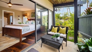 A bedroom with a bed, a glass door leading to a balcony with a wicker chair and a table.