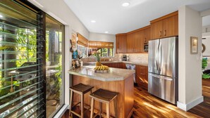 A modern kitchen with wooden cabinets, a stainless steel refrigerator, and a central island with stools.
