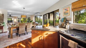 A modern kitchen with a large island, wooden cabinets, and a dining area with wicker chairs.