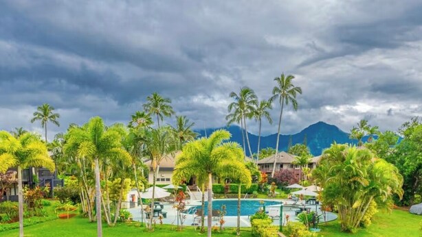 A resort with a pool surrounded by palm trees and a mountain in the background.