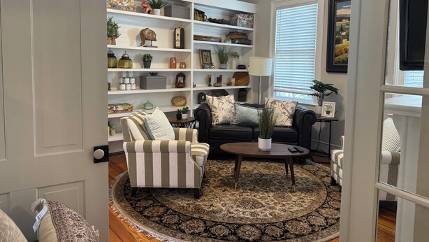A living room with a sofa, armchairs, a coffee table, and a patterned rug. There is a bookshelf filled with various decorative items and a ceiling fan. - Charming Century Old 3-bedroom house with WiFi and AC in fantastic Columbia (Columbia)