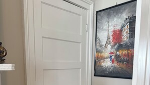 A room with a white door, a painting of a rainy street scene, a bed with a pink blanket, and a vintage suitcase. - Charming Century Old 3-bedroom house with WiFi and AC in fantastic Columbia (Columbia)