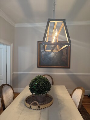 A dining area with a wooden table, chairs, a hanging light fixture, and a framed artwork on the wall.