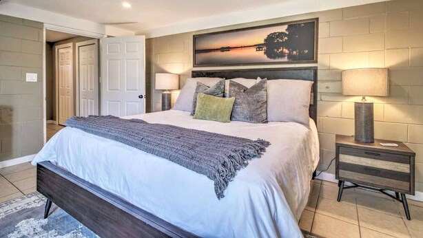 A bedroom with a large bed, two bedside tables, a nightstand, a painting on the wall, and a door leading to another room.