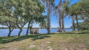 A lakeside property with a small cabin, surrounded by tall trees and grassy areas.