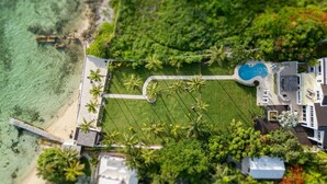 Vue aérienne d’un complexe hôtelier doté d’une piscine, d’une plage et d’une végétation luxuriante.