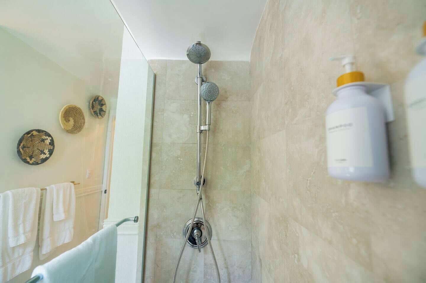 A bathroom with a glass-enclosed shower, a towel rack with white towels, and a wall-mounted soap dispenser.
