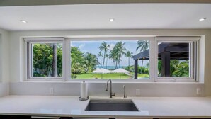 Une cuisine dotée d’une grande fenêtre donnant sur un paysage tropical, avec des palmiers et une piscine.