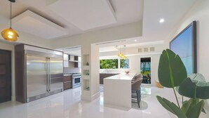 Une cuisine moderne dotée d’appareils électroménagers en acier inoxydable, d’un îlot central et de luminaires suspendus.