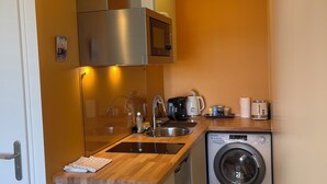 Een kleine keuken met een ingebouwde magnetron, een koffiezetapparaat, een broodrooster en een wasmachine.
