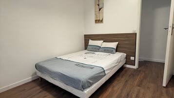 Ein Schlafzimmer mit Holzboden, einem Bett mit grau-weißer Matratze, einem Holz-Kopfende und einem an der Wand befestigten Rosenbild.