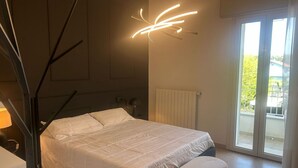Une chambre à coucher comprenant un lit, une table de chevet, une lampe, un radiateur et une porte-fenêtre coulissante donnant sur l’extérieur.