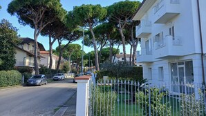 Une rue résidentielle bordée d’arbres, avec des voitures garées, un immeuble blanc doté de balcons.