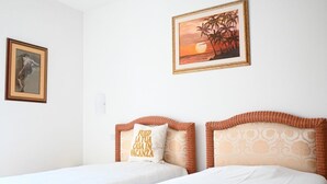Une chambre d’hôtel avec deux lits, un tableau encadré représentant une danseuse et une scène de coucher de soleil.