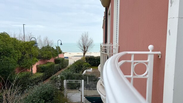 Un balcon donnant sur une plage et une porte menant à un sentier.