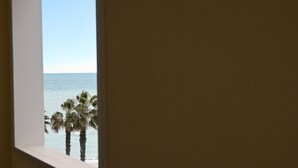 Une vue à travers une fenêtre, avec un ciel dégagé, une plage et des palmiers.