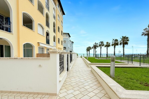 A multi-story building with balconies, a tiled pathway, and a view of the sea.