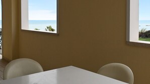 Une pièce comprenant une table et deux chaises, une fenêtre donnant sur la mer et un balcon avec une balustrade.