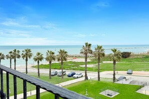 A coastal view with a parking area, palm trees, and a clear sky.