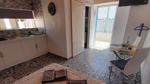 A cozy room with a wooden ceiling, a kitchen area with a sink and cabinets, a dining table with chairs, and a patterned floor. - Tropicana Holiday Apartments (Albufeira)