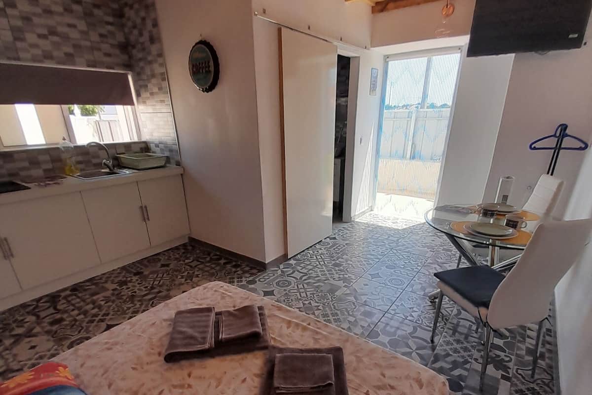 A cozy room with a wooden ceiling, a kitchen area with a sink and cabinets, a dining table with chairs, and a patterned floor.