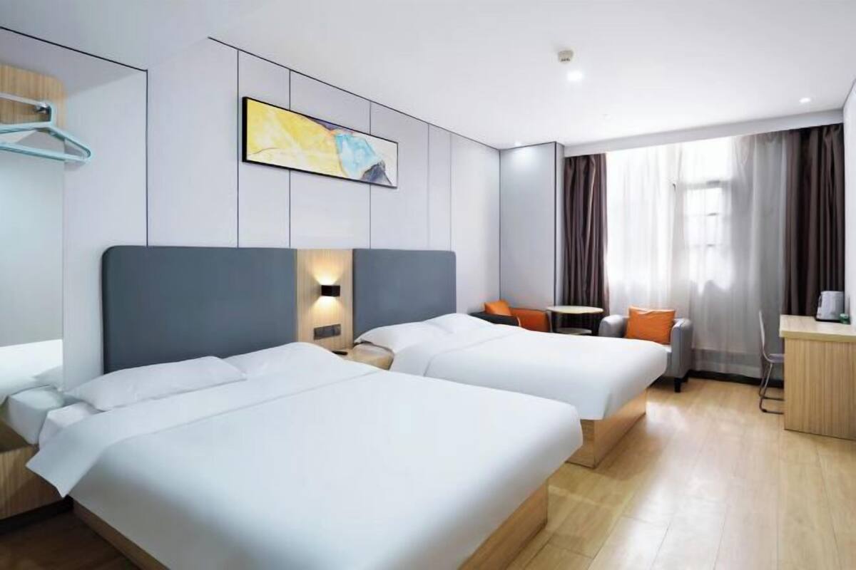A hotel room with two beds, a desk, a chair, a small table, and a painting on the wall.