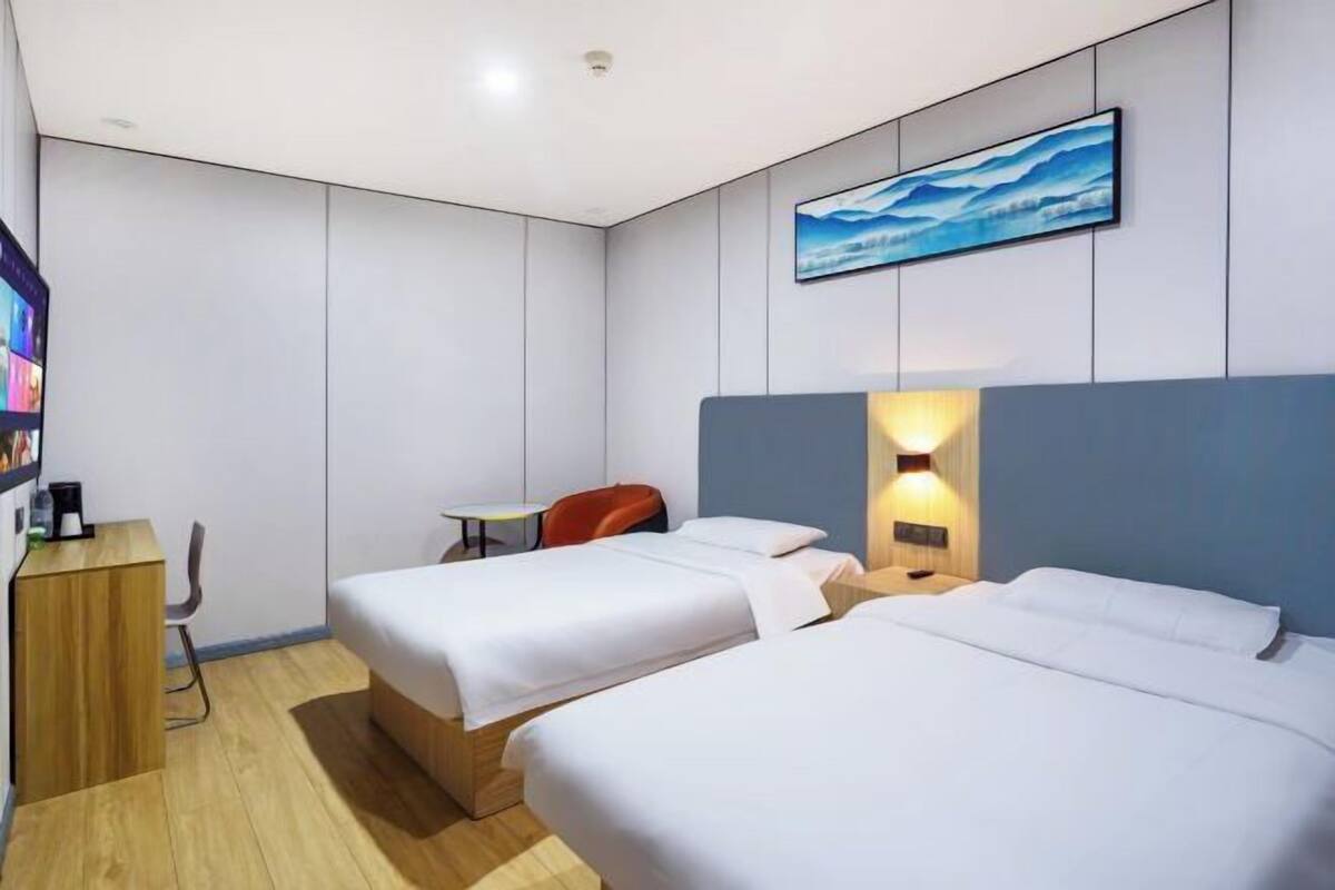A modern hotel room with two beds, a desk, a chair, and a bookshelf.