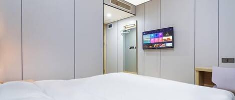Une chambre d’hôtel moderne avec un grand lit, un téléviseur fixé au mur et un miroir.