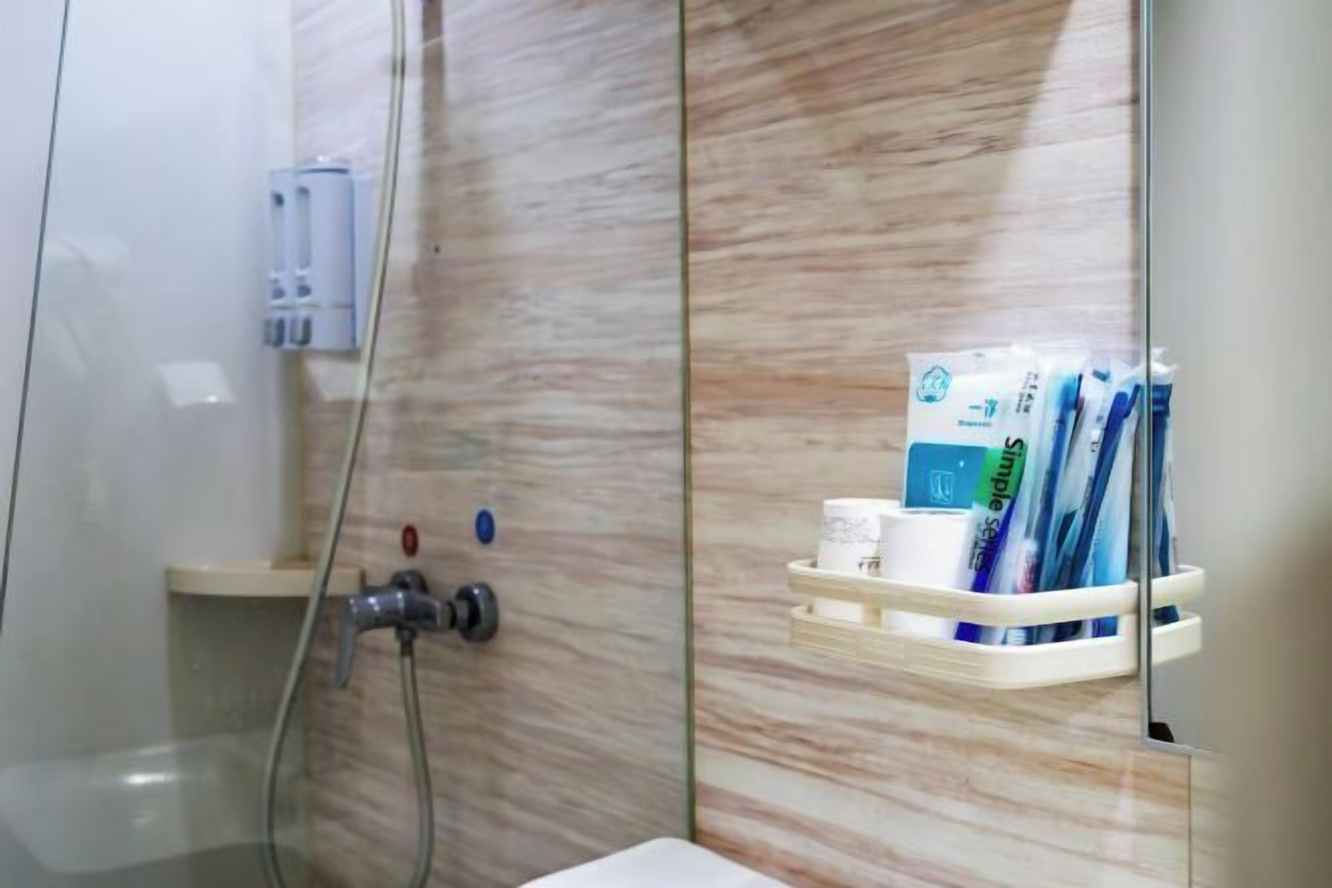 Ein Badezimmer mit Duschkabine aus Glas, einem weißen Waschbecken und Ablagefläche für Pflegeprodukte.