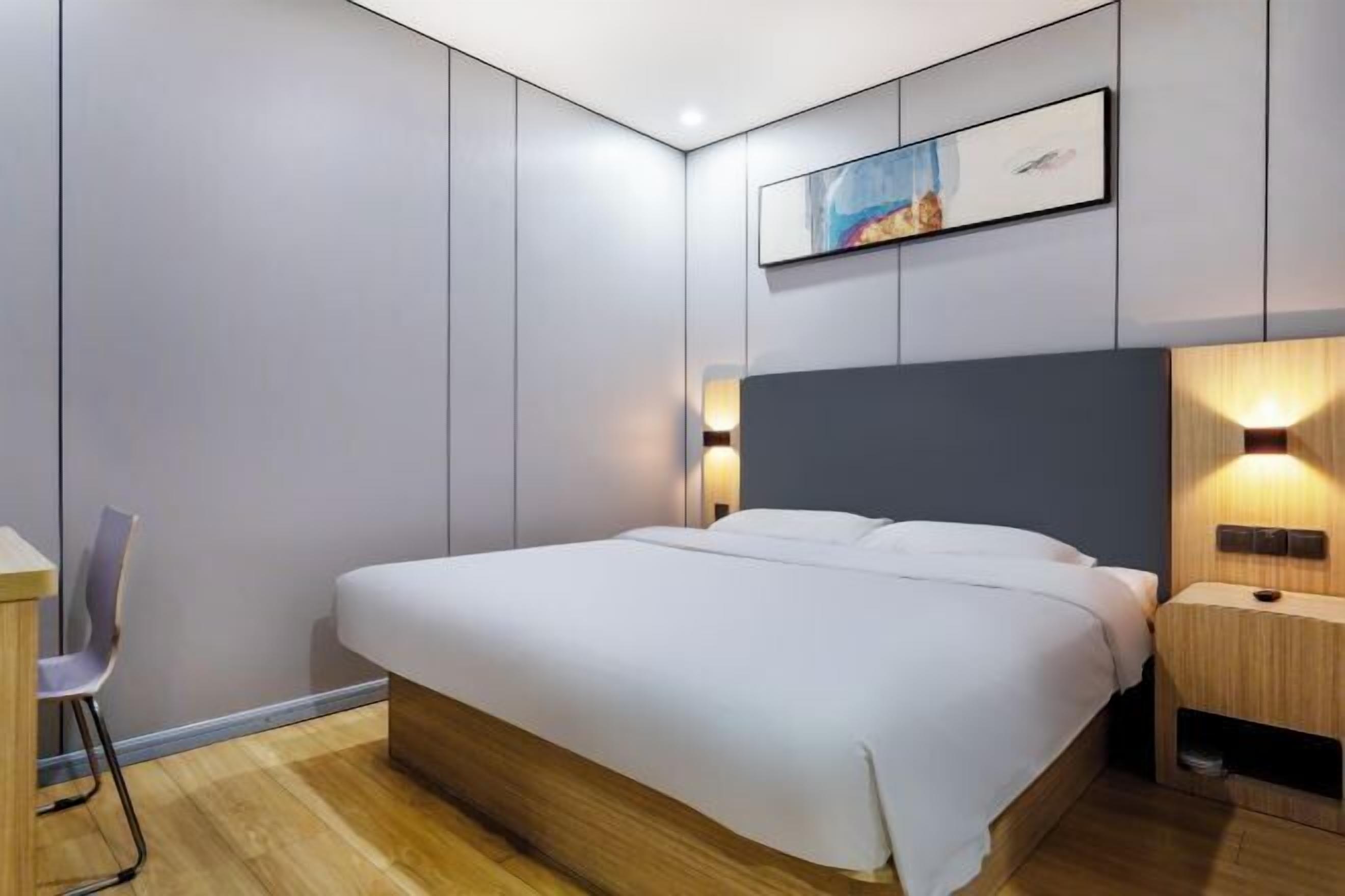 A modern bedroom with a large bed, bedside tables, a chair, and a wall-mounted artwork.