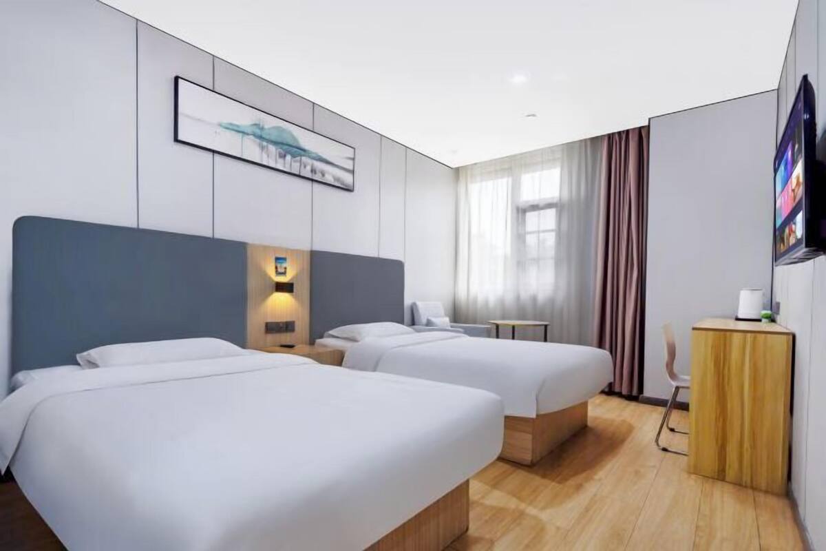 A hotel room with two beds, a TV, a desk, and a window with curtains.