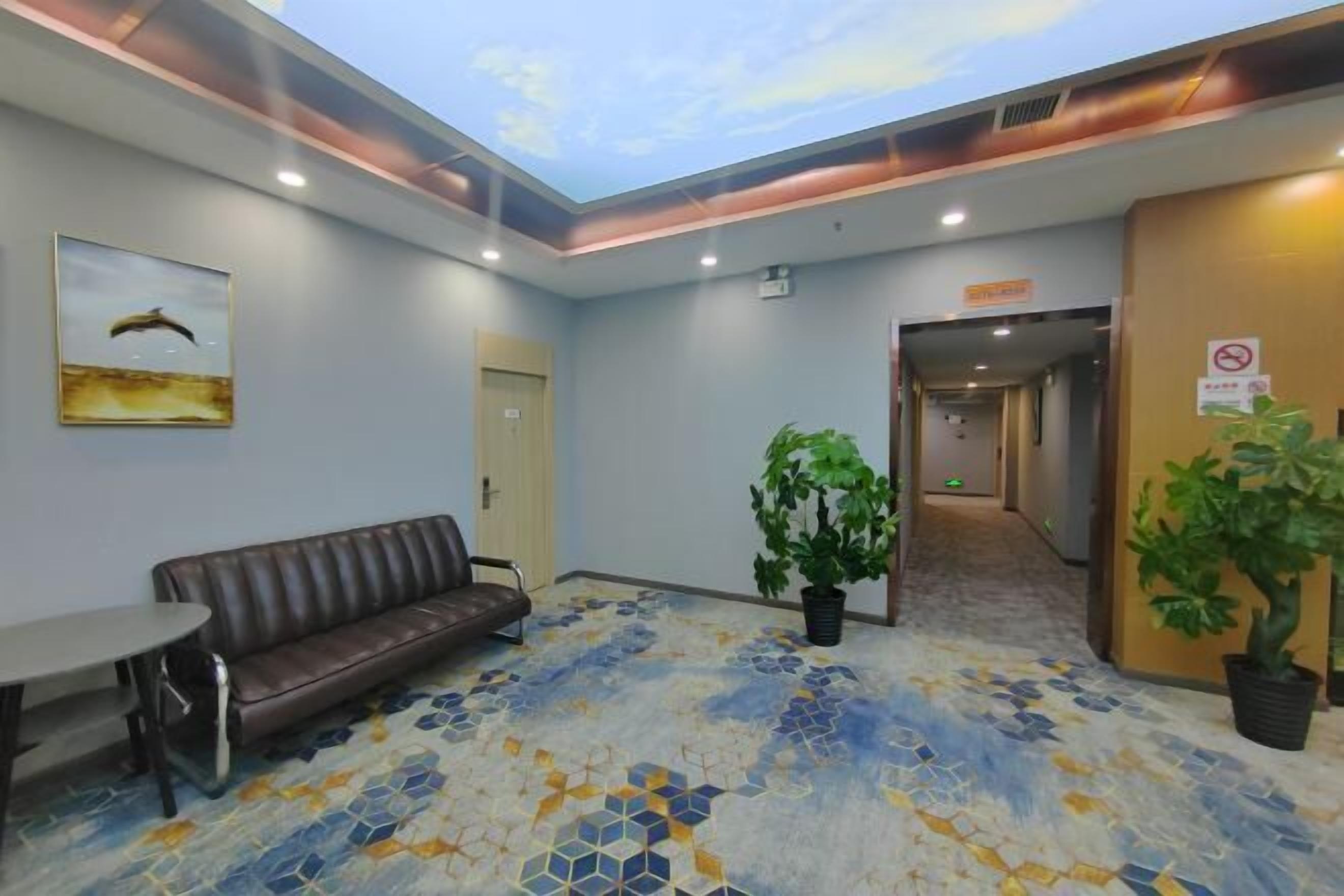 A lobby with a ceiling mural, a brown leather sofa, a round table, and potted plants.