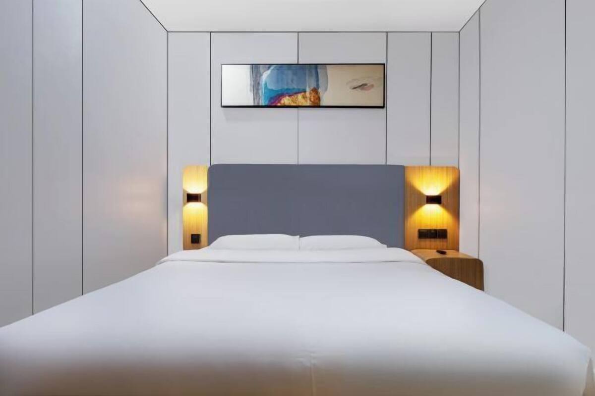 A modern bedroom with a large bed, two bedside lamps, and a framed artwork on the wall.