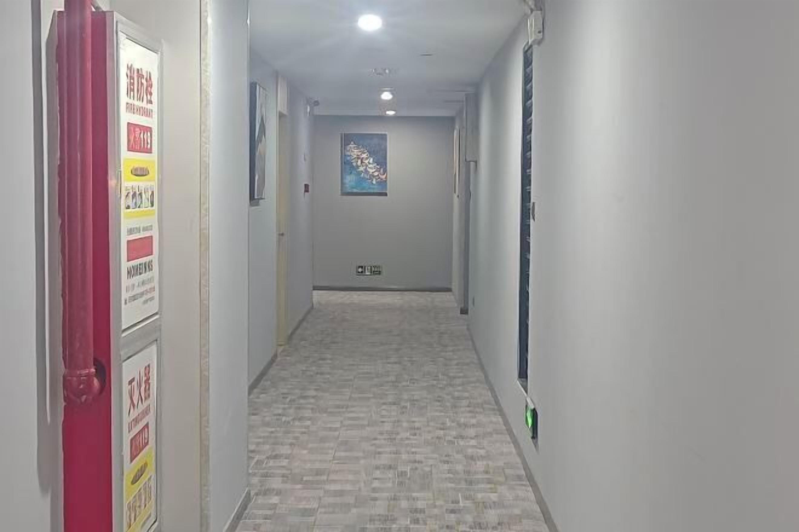 A hallway with tiled flooring, a red door on the left, and a poster on the wall.