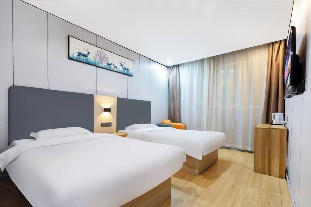 A hotel room with two beds, a flat-screen TV, a painting on the wall, and a wooden side table.