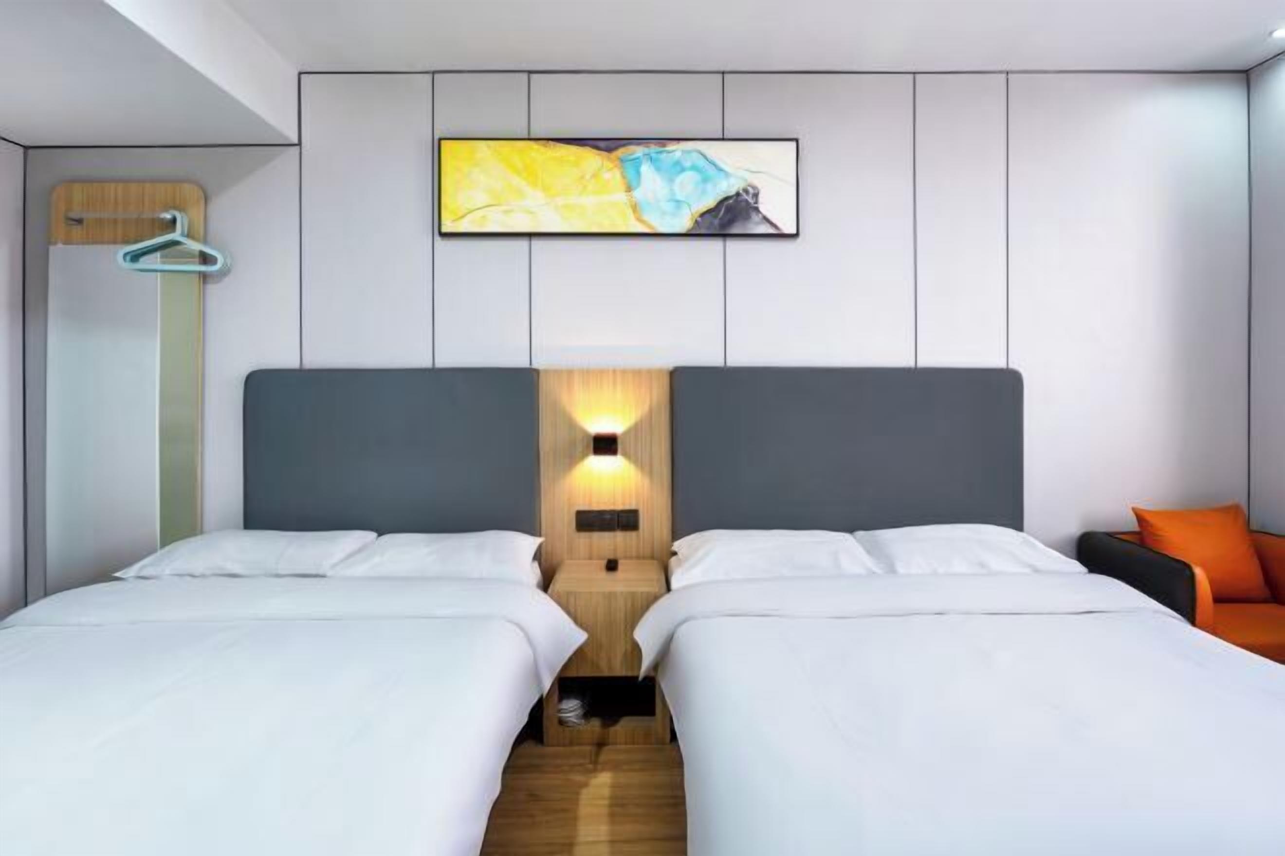 A hotel room with two beds, a wooden headboard, a wall-mounted artwork, and a side table with a lamp.