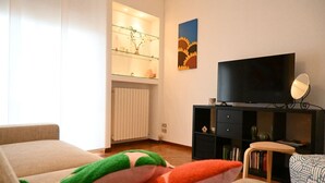 Een woonkamer met een bank, een televisie, een boekenkast en een radiator.