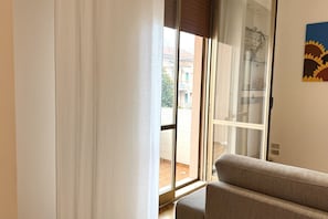 Ein Zimmer mit einer Schiebeglastür, die zu einem Außenbereich führt, einer Couch und einem an der Wand hängenden Kunstwerk.